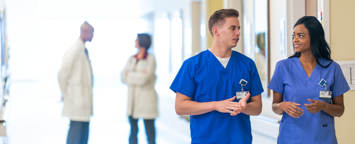 Nurses walking down a hallway talking with doctors in the background