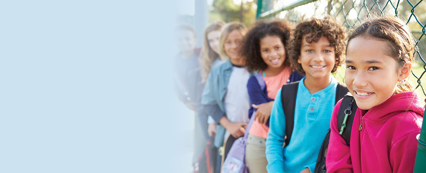 Group of kids leaning against playground fence. 