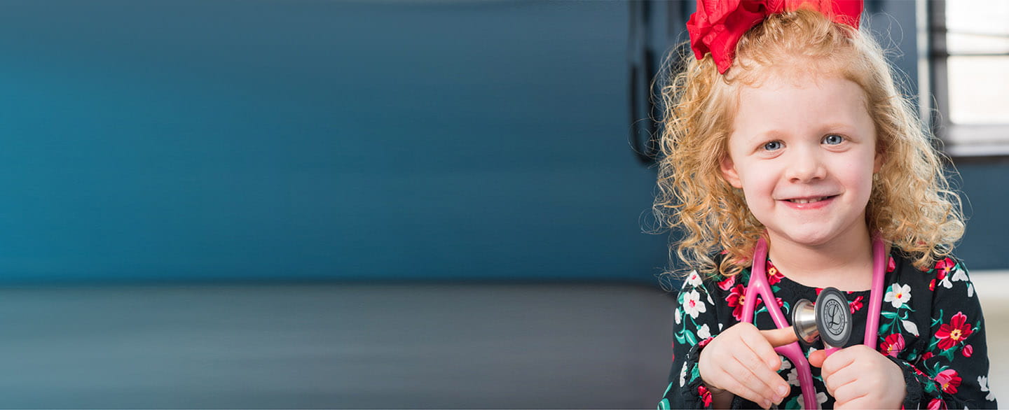 Little girl wearing stethoscope smiling.