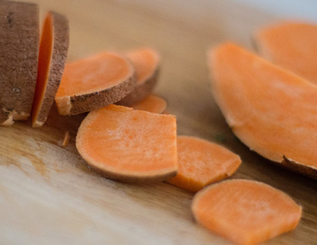 Sweet potato and slices on a wooden cutting board.