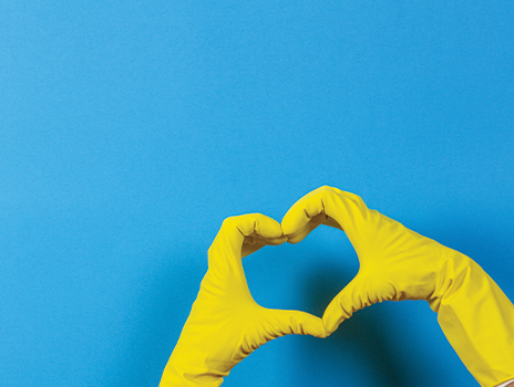 Hands wearing yellow cleaning gloves making a heart on a solid blue background