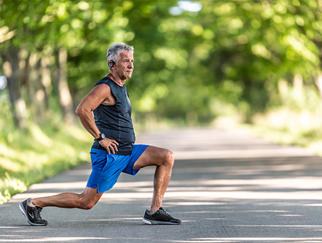 Older man outside on a bright shady trail stretching before he runs