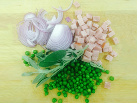 Chopped ham, onions and peas on cutting board.