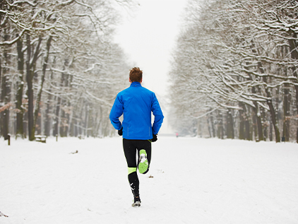 Person jogging down a snowy path in-between a line of trees