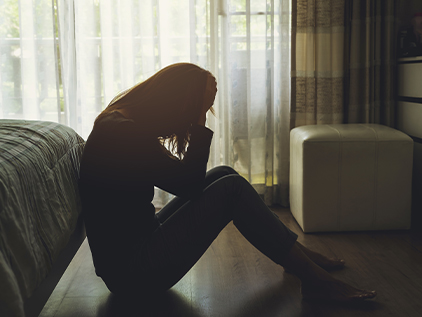Depressed woman sitting on her bedroom floor with her head in her hands