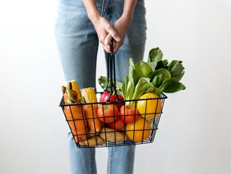 Woman holding a grocery basket full of vegetables.