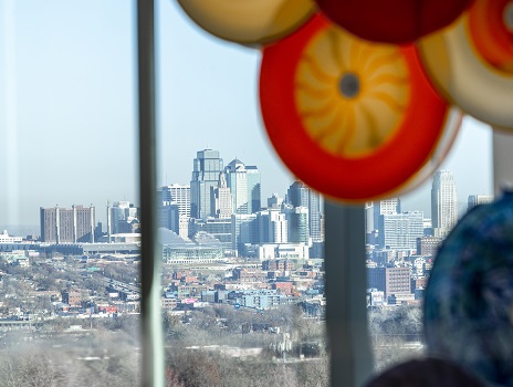 Orange and yellow glass circles hang in front of 3 large windows overlooking downtown Kansas City, MO