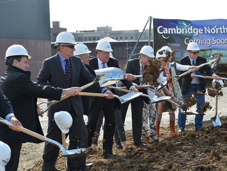 Individuals wearing white hardhats throw shovels of dirt at the groundbreaking ceremony for Cambridge Tower A