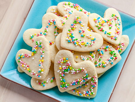 Plate of heart shaped cookies with sprinkles.