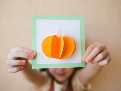 little girl holding a paper pumpkin