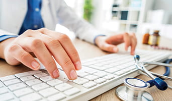Hands of a doctor typing on a keyboard.