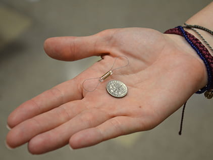 Someone holding the CardioMEMS device showing it is no bigger than a dime.