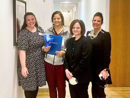 Daniela Whyte, holding blue folder, stands with 3 nursing leaders to celebrate her RFTS scholarship.
