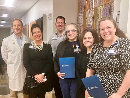 Marcia Petty, wearing glasses and holding a blue folder, stands with members of nursing leadership and Infectious Disease to celebrate her RFTS scholarship.