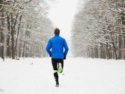 Person jogging down a snowy path in-between a line of trees